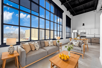 A modern living room with a grey sofa, wooden coffee table, and a large window.